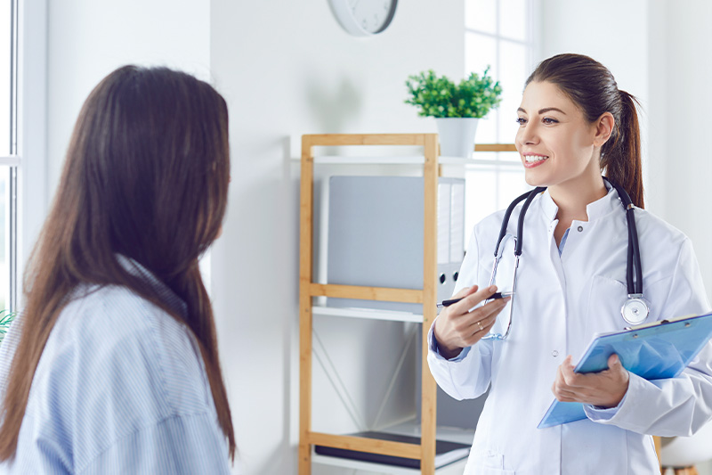Physician speaking to a patient, physician is holding a blue clipboard.